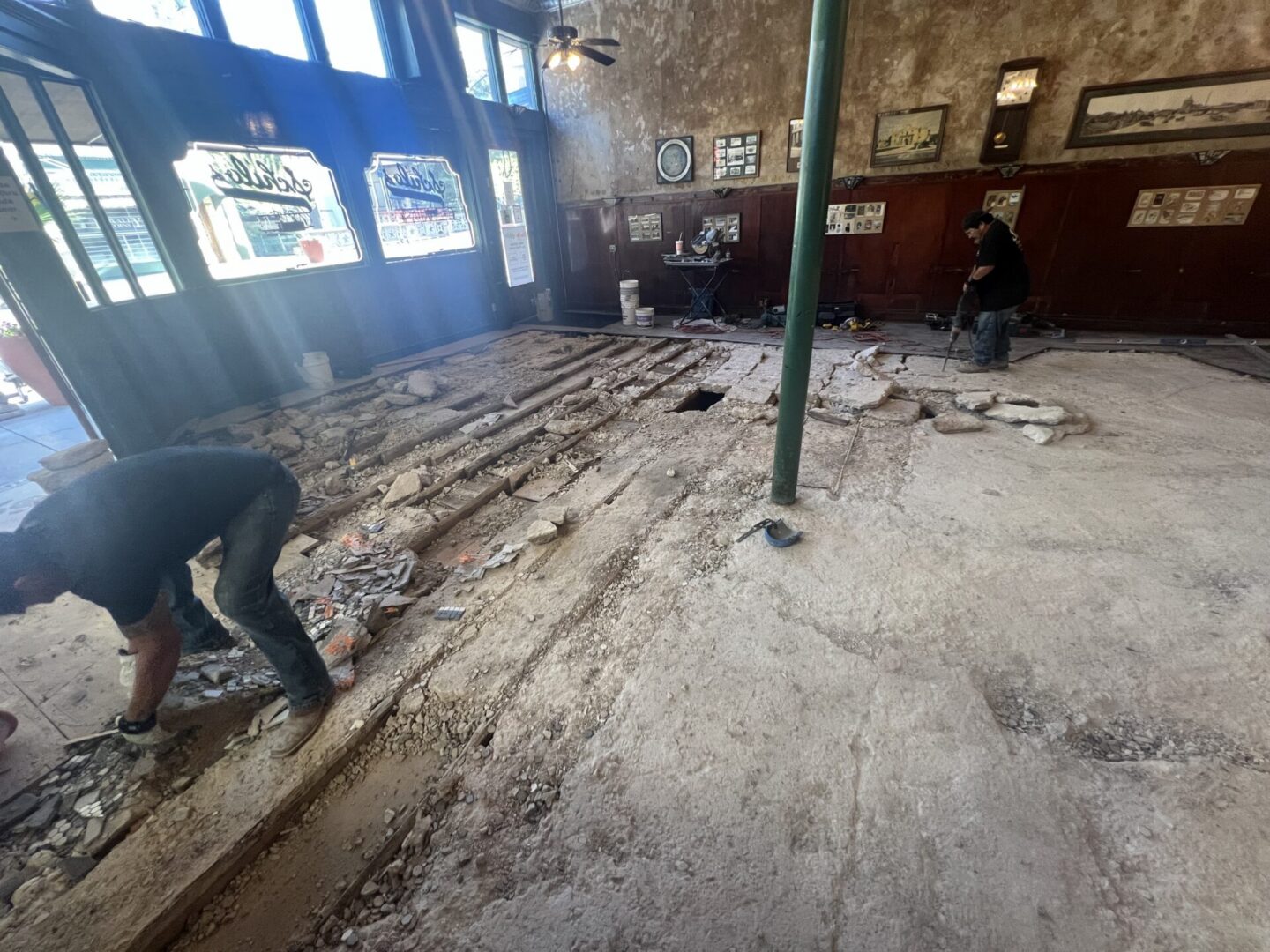 Workers remove debris from a floor in preparation for installing Metallic Epoxy Flooring in a construction project.