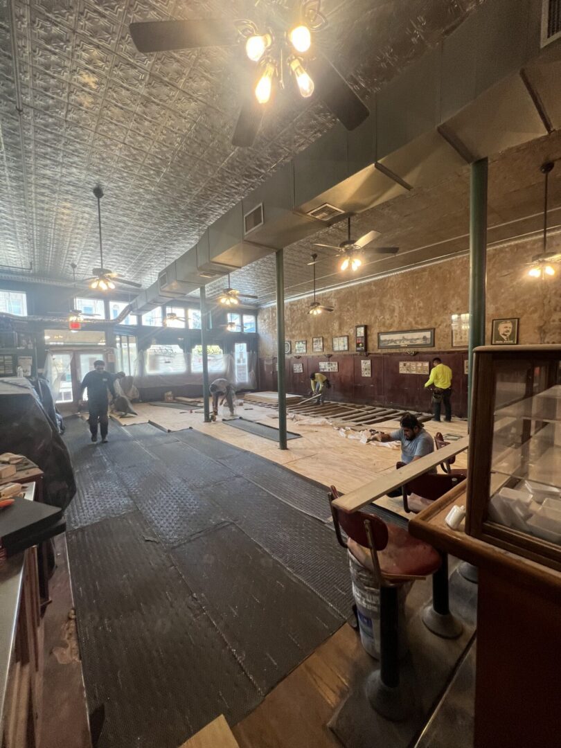 Workers install flooring in a restaurant, preparing for Metallic Epoxy Flooring amidst a vintage interior.