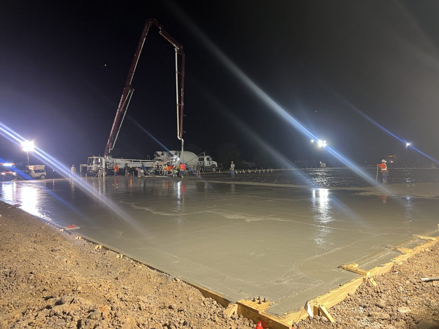 Construction workers pour concrete at night, preparing a surface for Metallic Epoxy Flooring installation.