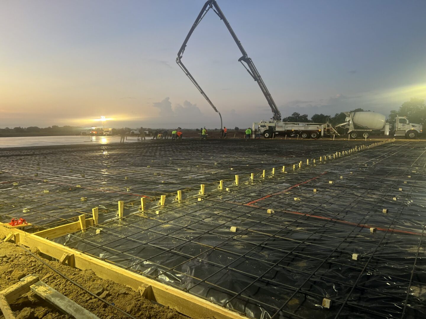 Construction workers pour concrete for a foundation, preparing for Metallic Epoxy Flooring installation at sunset.