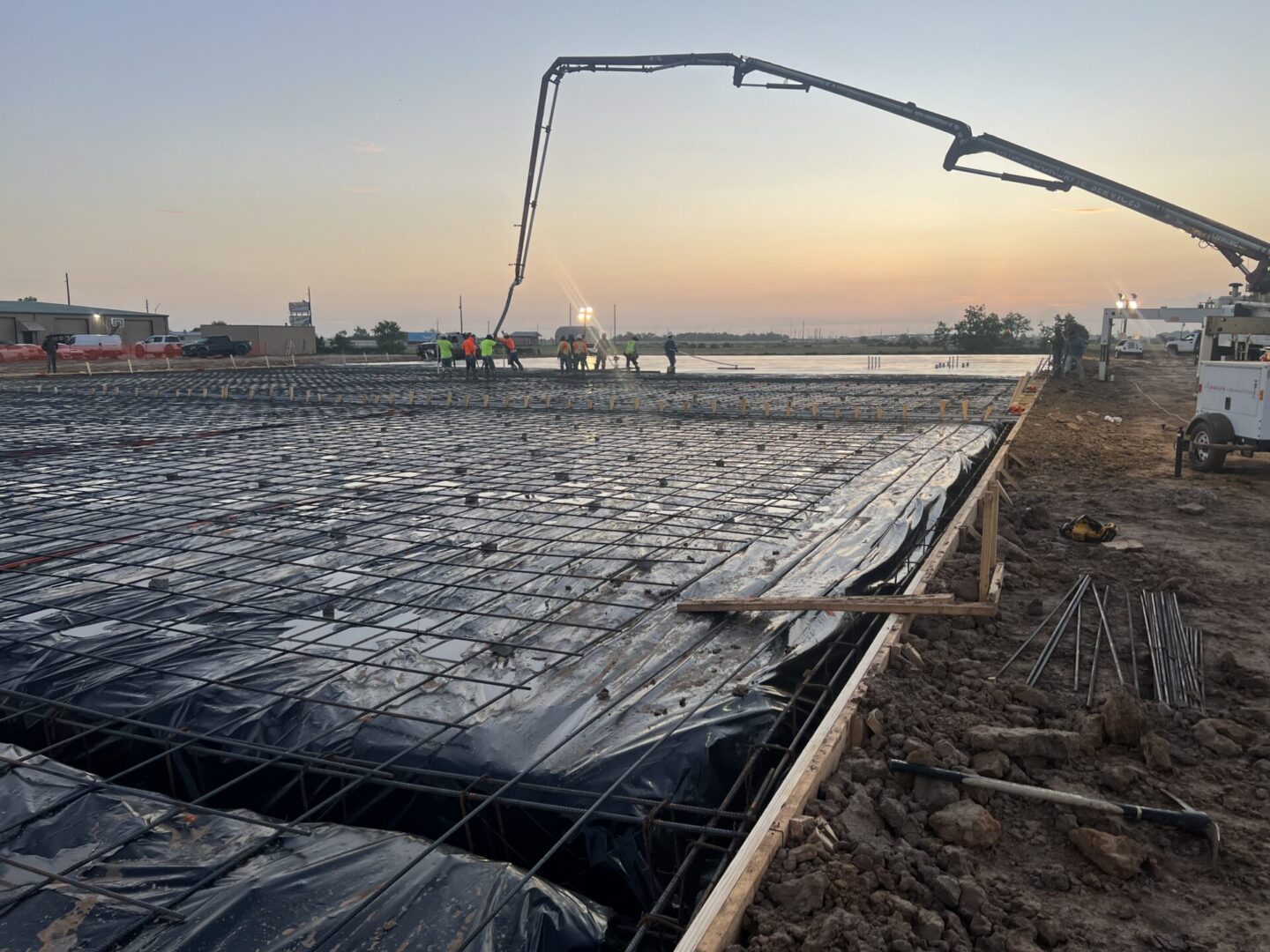 Construction workers pour concrete on a large foundation, preparing for Metallic Epoxy Flooring installation at sunrise.