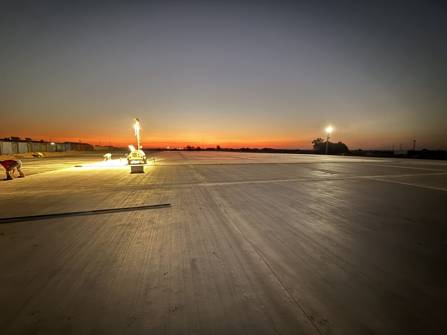 Construction workers apply finishing touches to a large concrete surface at sunset, highlighting the potential for Metallic Epoxy Flooring.