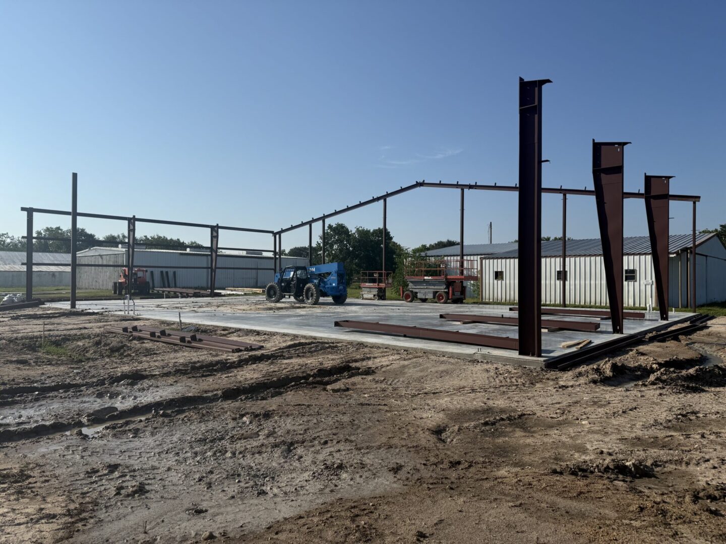 Construction site featuring steel framework for a building, with machinery and materials for Metallic Epoxy Flooring installation.