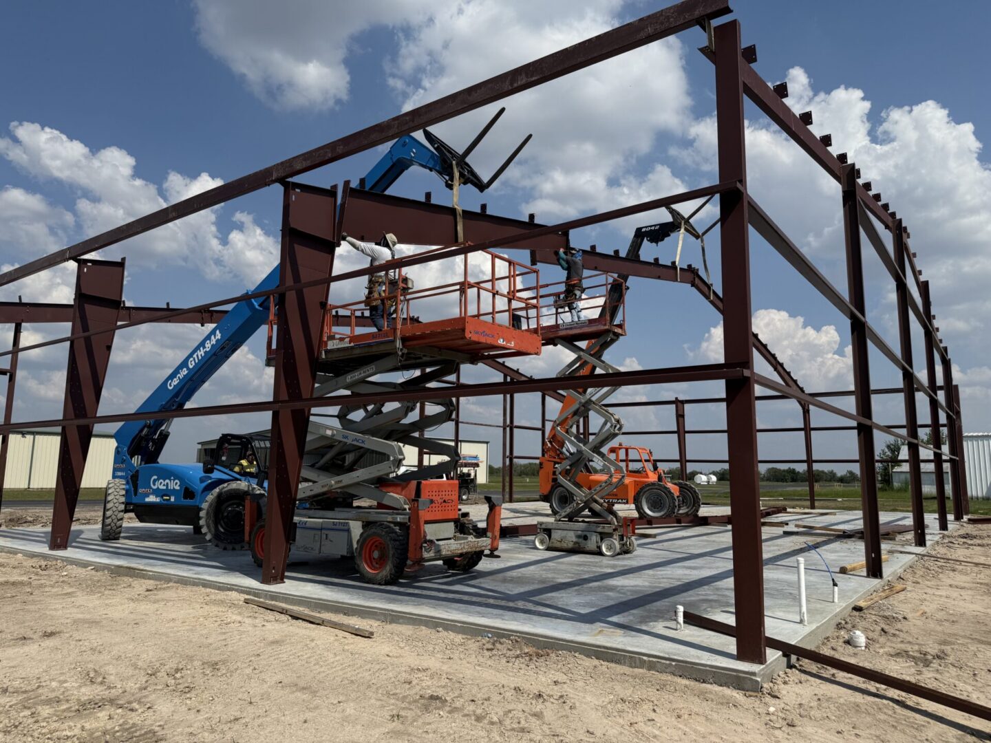 Construction site featuring machinery and workers installing a steel frame, highlighting the future application of Metallic Epoxy Flooring.