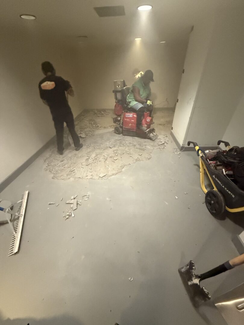 Workers grinding concrete floor in small room